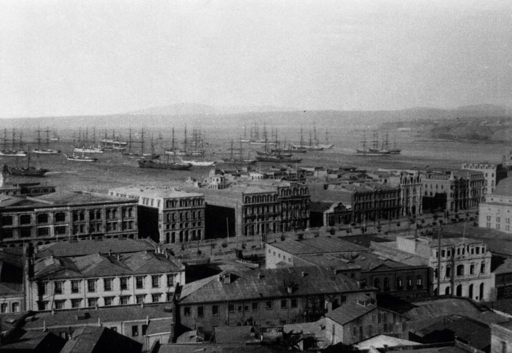 Vista aérea en blanco y negro de Valparaíso mostrando edificios históricos, puerto con embarcaciones y cerros al fondo