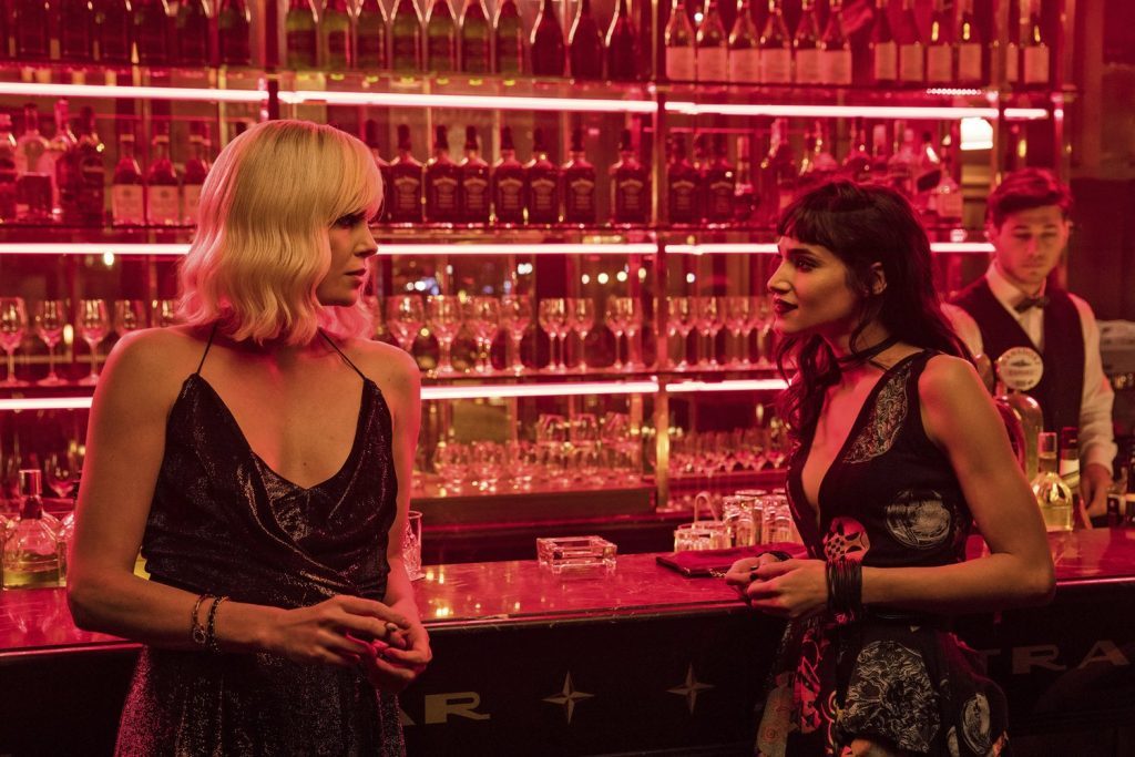 Dos mujeres en un bar con iluminación roja neon conversan junto a la barra, ambiente de película de acción