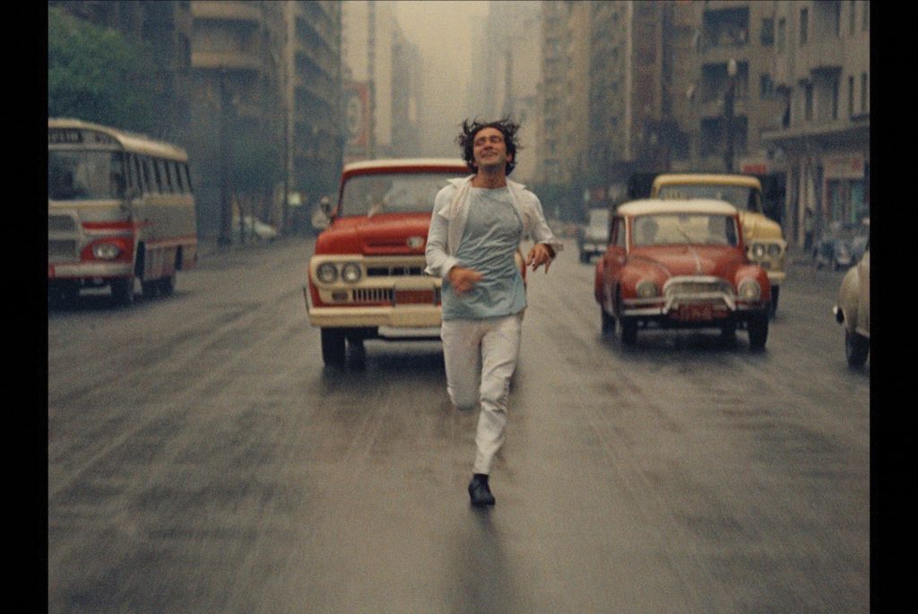 Hombre corriendo por calle urbana entre autos antiguos en ciudad brasileña de los años 60