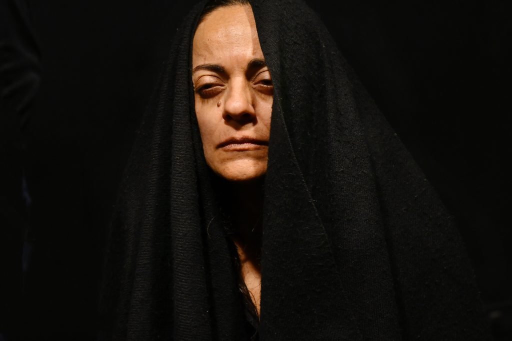Violeta Parra con la cabeza cubierta por un velo negro, expresión seria, iluminación dramática sobre fondo oscuro