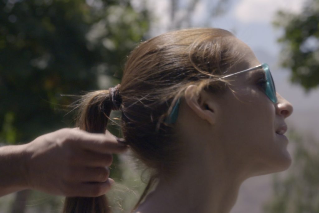 Mujer de perfil recogiendo su cabello rubio hacia atrás, luz natural de día, ambiente exterior