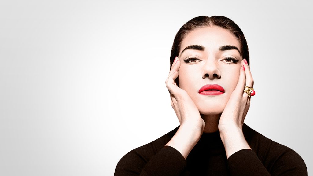 "La Divina" María Callas: La soprano del amor y de la muerte María Callas con maquillaje dramático, manos en el rostro, expresión contemplativa sobre fondo gris claro