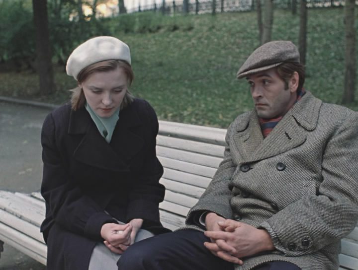 "Una blanca revelación": En invierno en Moscú... hace frío (y nieva) Dos hombres sentados en un banco de parque conversando, él con abrigo gris y gorra, ella con abrigo negro y boina