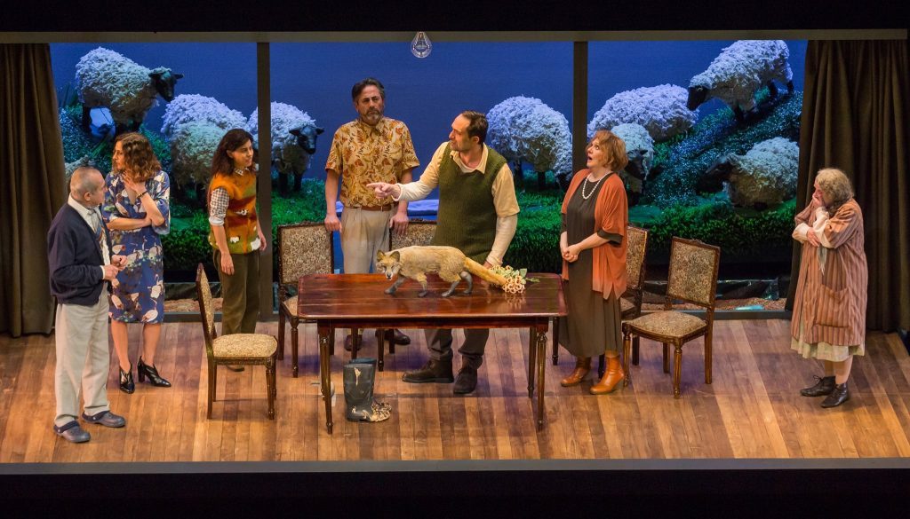 Escena teatral con actores en sala de estar, muebles de época y decoración azul al fondo, adaptación de obra de Chéjov