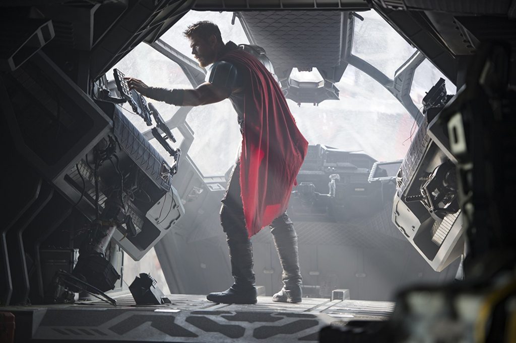 Personaje de Thor con capa roja asomado por ventana de nave espacial, ambiente oscuro y desolado de destrucción
