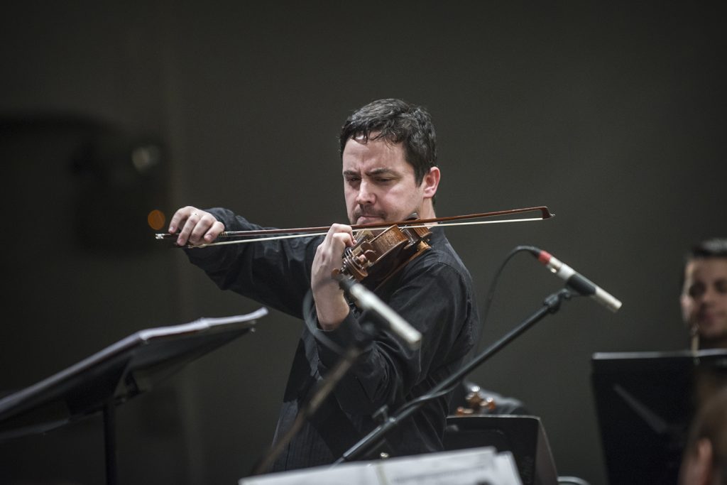 Violinista en intenso solo, sostiene su instrumento con expresión concentrada durante presentación en escenario