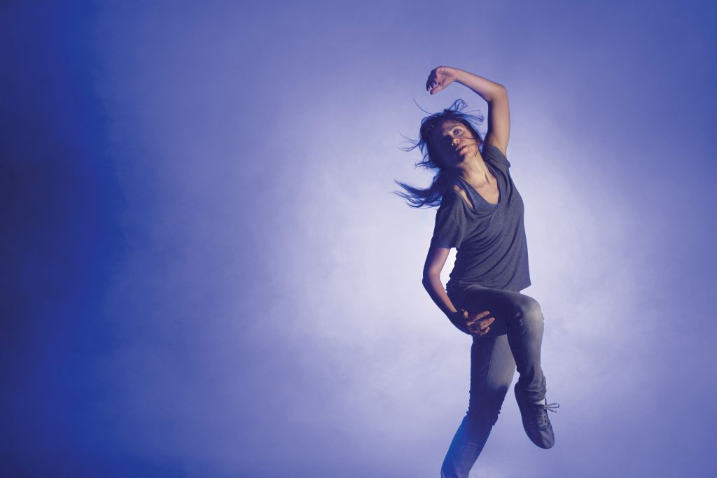 Bailarina saltando en el aire con los brazos levantados contra fondo azul degradado iluminado