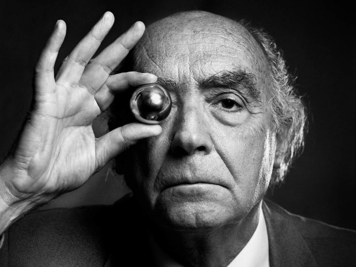 José Saramago sostiene una lupa frente a su ojo izquierdo, retrato en blanco y negro de perfil