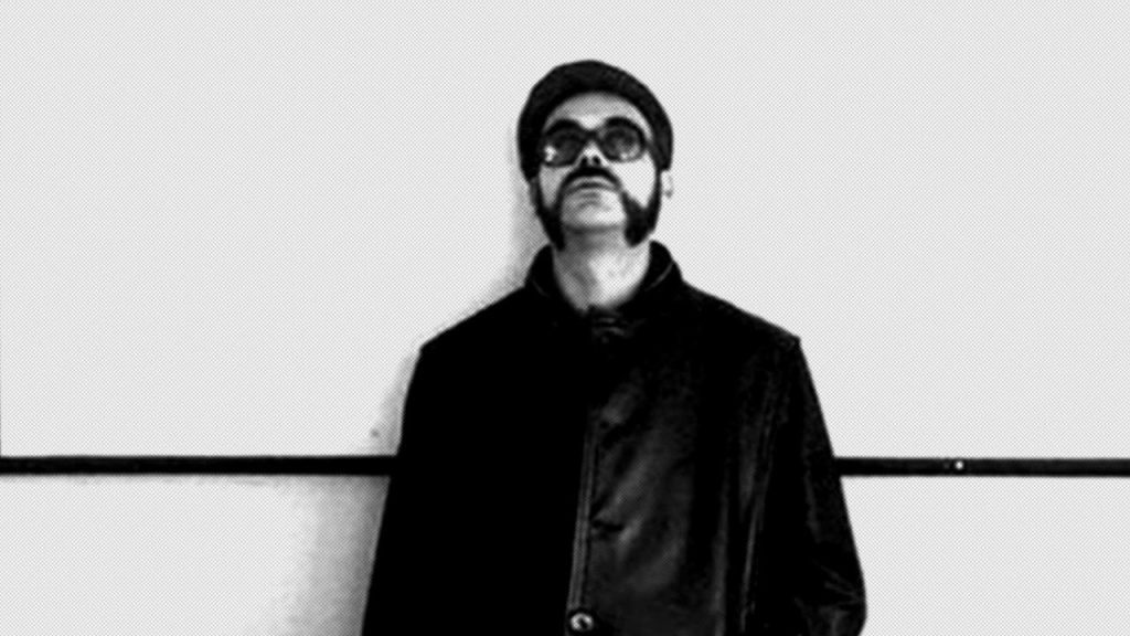 Retrato en blanco y negro de Rodrigo Lira, poeta chileno con gafas oscuras, chaqueta negra y bigote, mirando