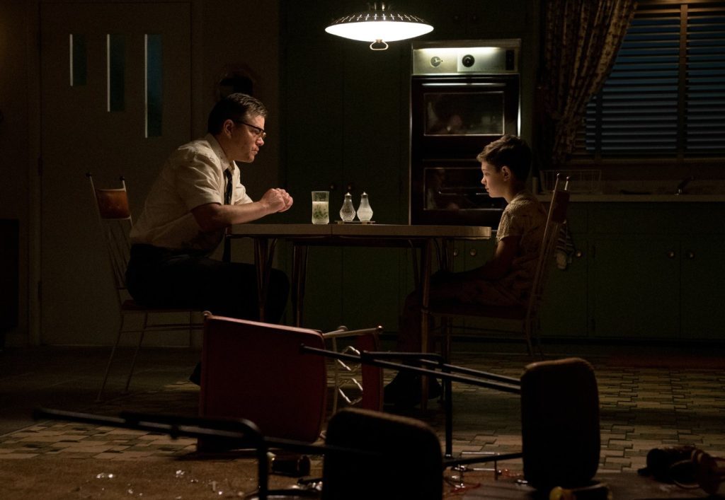 “Suburbicon: Bienvenidos al paraíso”, el bosque del odio Dos hombres en una sala oscura iluminada por luz tenue, sentados frente a frente en una tensa conversación nocturna