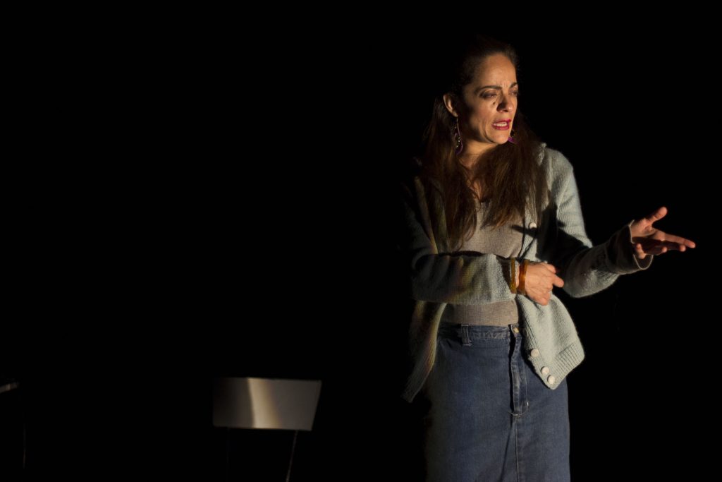 "Hilda Peña": Una poética de la desesperación Hilda Peña en escena teatral, con expresión contemplativa, iluminada contra fondo oscuro, gesticulando con la mano