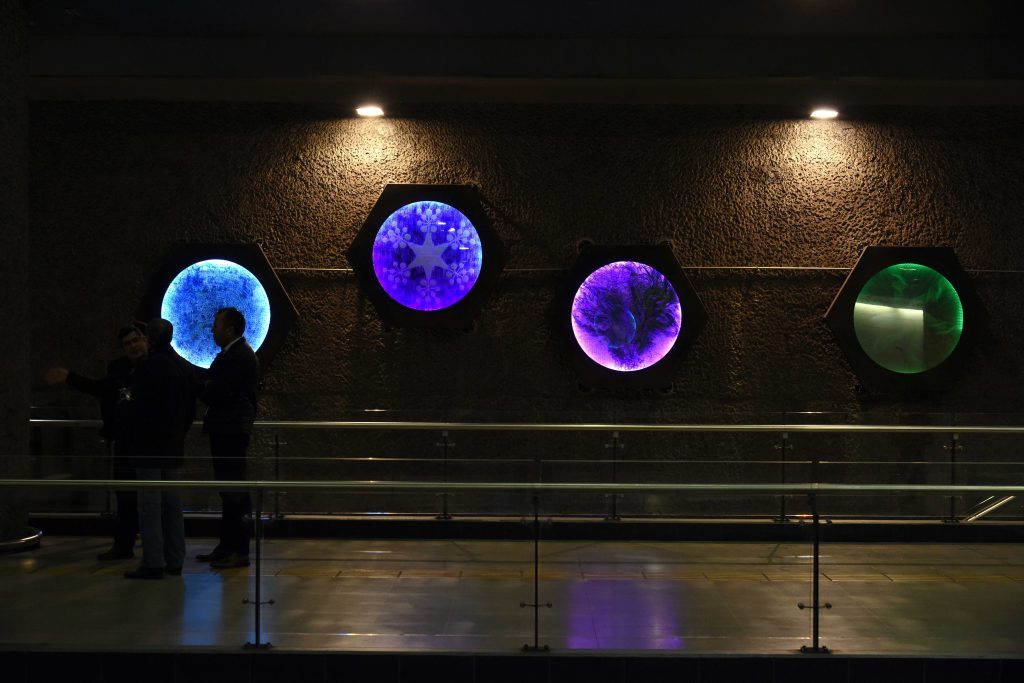Cuatro esferas luminosas de colores azul, púrpura y verde en mural electrónico dentro de estación de Metro