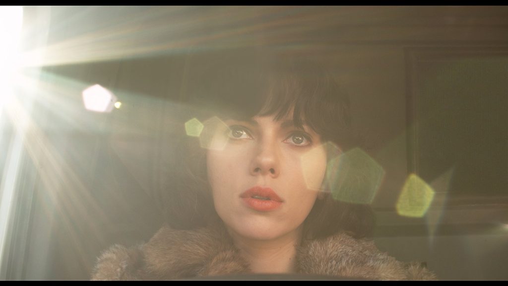Mujer joven con cabello oscuro y flequillo, iluminada por luces de neón en tonos amarillos y verdes en ambiente oscuro