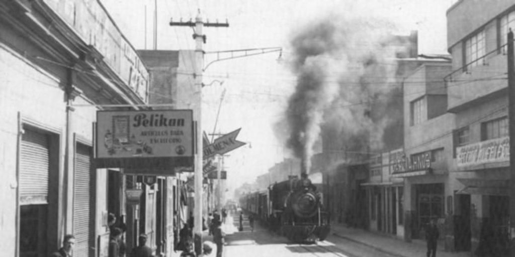 Calle de Coquimbo con edificios antiguos y locomotora a vapor expulsando humo, escena urbana chilena de principios