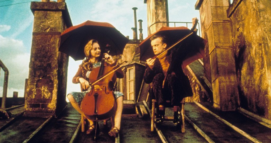 Tres músicos tocan instrumentos de cuerda en una calle estrecha entre edificios antiguos al atardecer