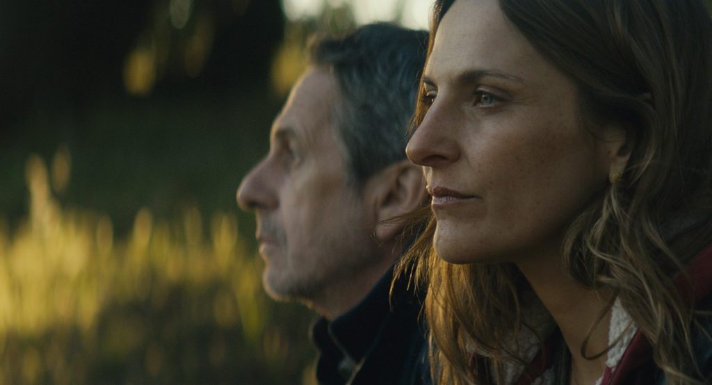Dos personas en perfil observan hacia el horizonte en un campo al atardecer, con luz dorada de fondo