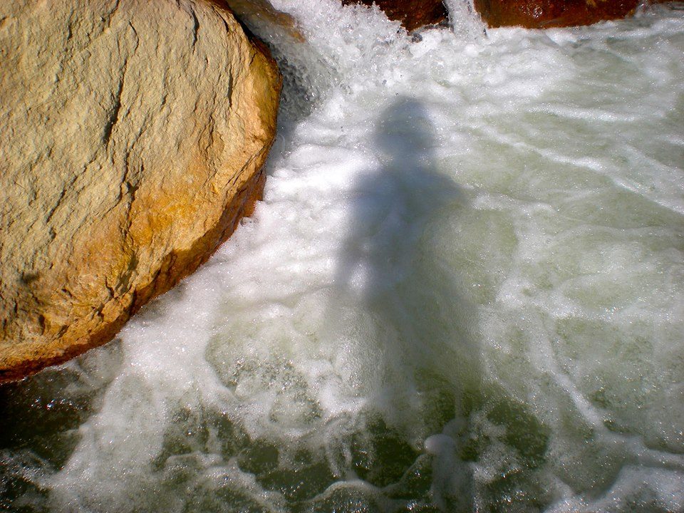 Exposición "Kura": El Mapocho, arteria mítica de la ciudad de Santiago Aguas turbulentas del río Mapocho con rocas ocres en primer plano, espuma blanca y corriente verde