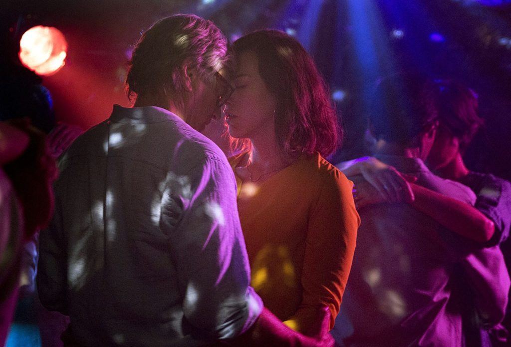 Pareja besándose en pista de baile con iluminación de neón rosa y azul, escena de intimidad nocturna