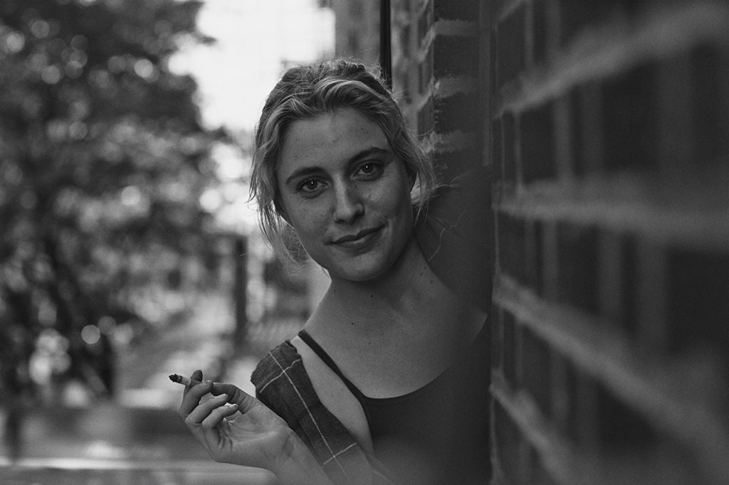 Alejandra Coz Rosenfeld apoyada en una pared de ladrillo, fumando, en fotografía en blanco y negro