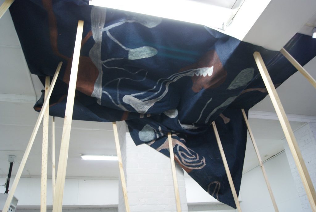Instalación de tela negra suspendida en estructura de madera blanca dentro de espacio expositivo iluminado