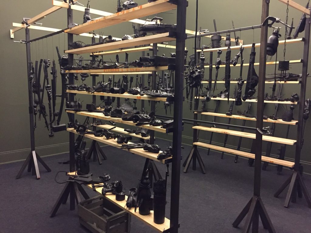 Exhibición de armas históricas y réplicas en vitrinas de metal, iluminadas contra fondo gris oscuro