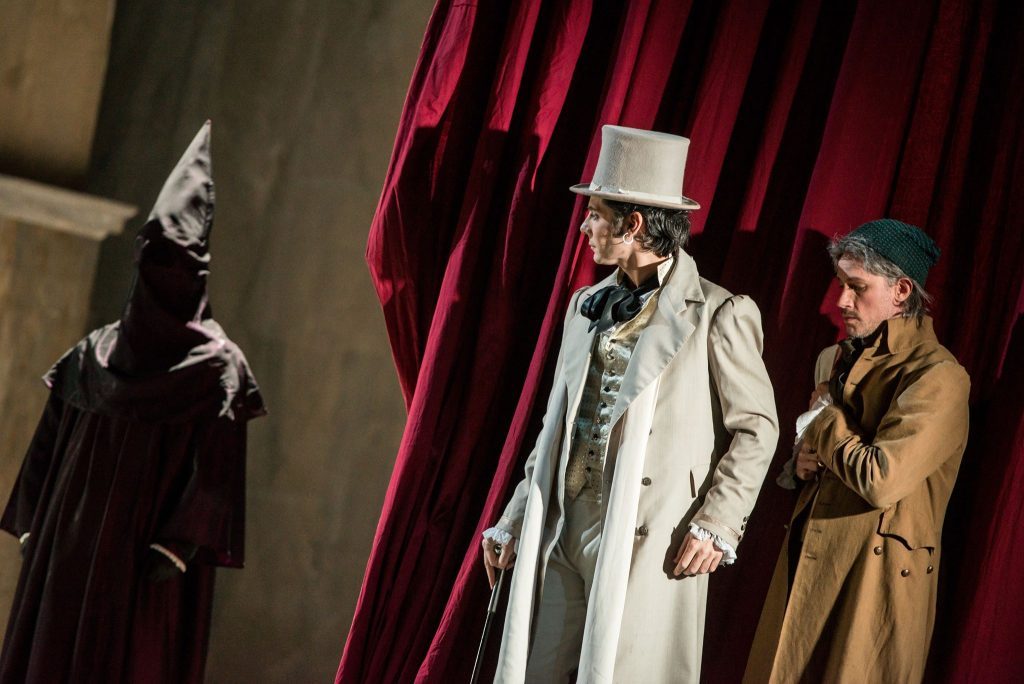 "Don Giovanni" de Mozart abre la temporada lírica 2018 del Teatro Municipal de Santiago Tres personajes en escena: uno de negro a la izquierda, otro con capa blanca y sombrero de copa en el centro