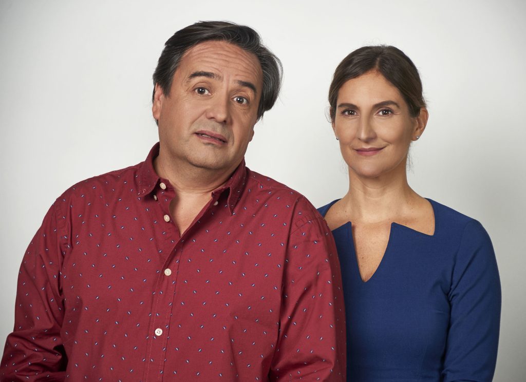 Dos personas frente a fondo blanco: hombre de camisa roja burdeos y mujer de blusa azul marino mirando hacia la cámara