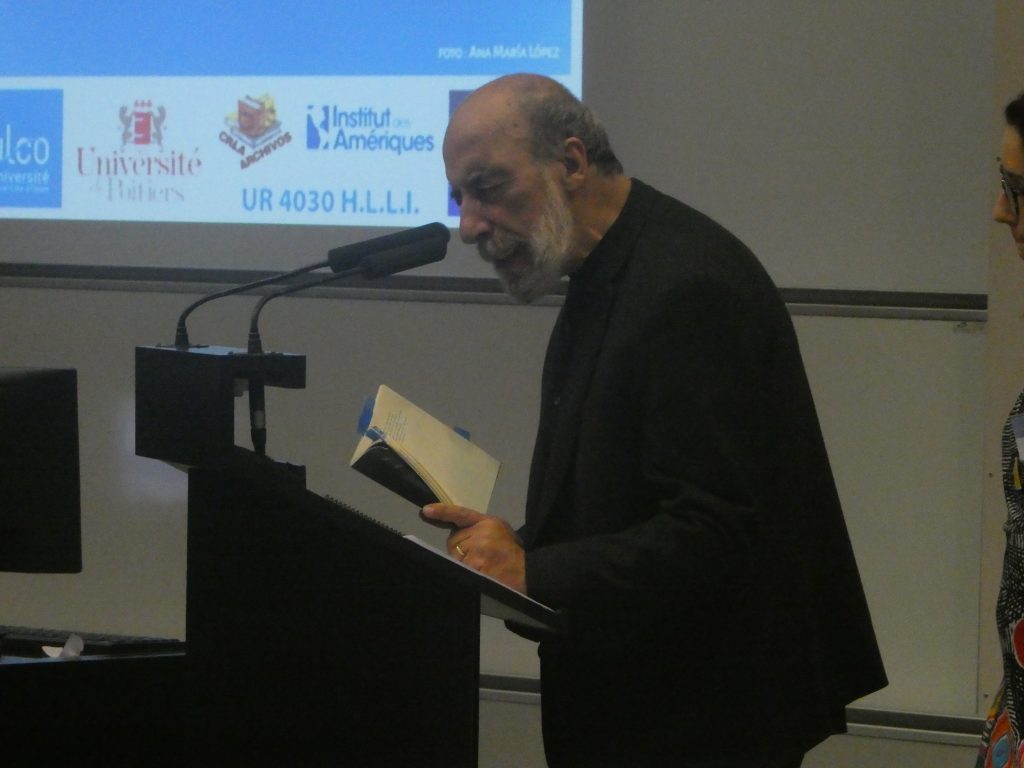 Raúl Zurita leyendo desde un podio durante presentación de su obra poética en universidad francesa