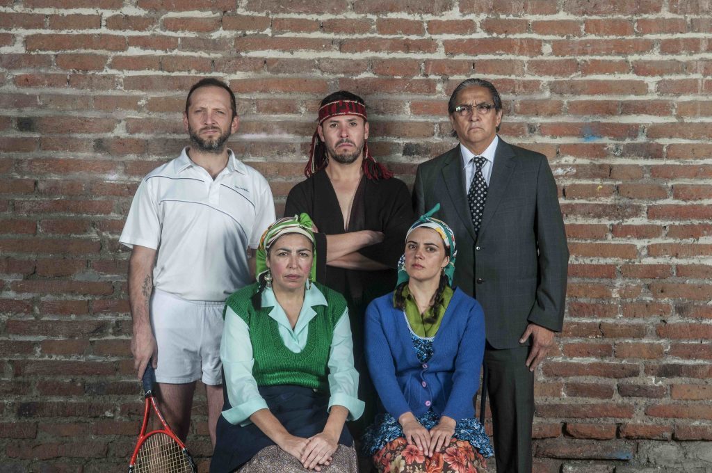 Cinco personas posando frente a pared de ladrillo: tres hombres de pie y dos mujeres sentadas, vistiendo ropa casual