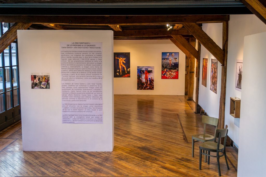 Entrevista: La transgresión impenitente del artista venezolano Nelson Garrido en la capital de Chile Galería de exposición con paneles informativos, fotografías de color en paredes blancas, piso de madera y vigas
