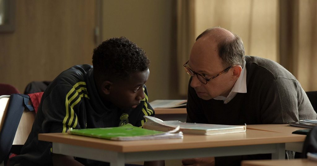 "El buen maestro", de Olivier Ayache-Vidal: Las transformaciones del amor Dos hombres en una sala de clase: uno afroamericano joven y otro mayor con gafas, inclinados sobre un escritorio