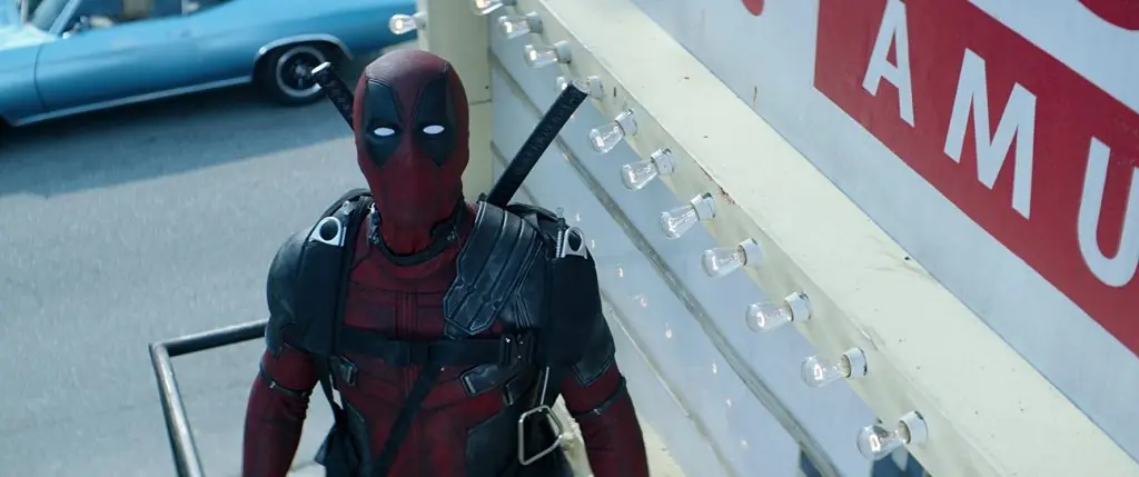 Personaje en traje rojo y negro con máscara facial sosteniendo una katana, de pie frente a un vehículo de emergencia