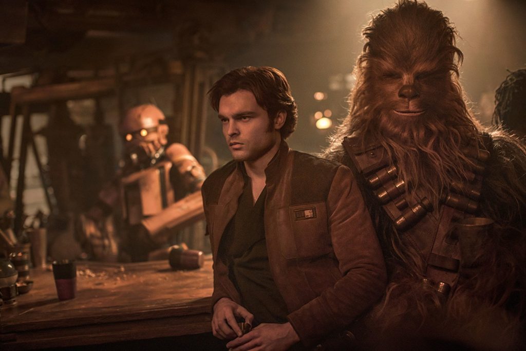 "Han Solo : Una historia de Star Wars": La rebelión de la orfandad Hombre joven en traje marrón junto a Chewbacca en interior iluminado cálidamente, escena de ciencia ficción