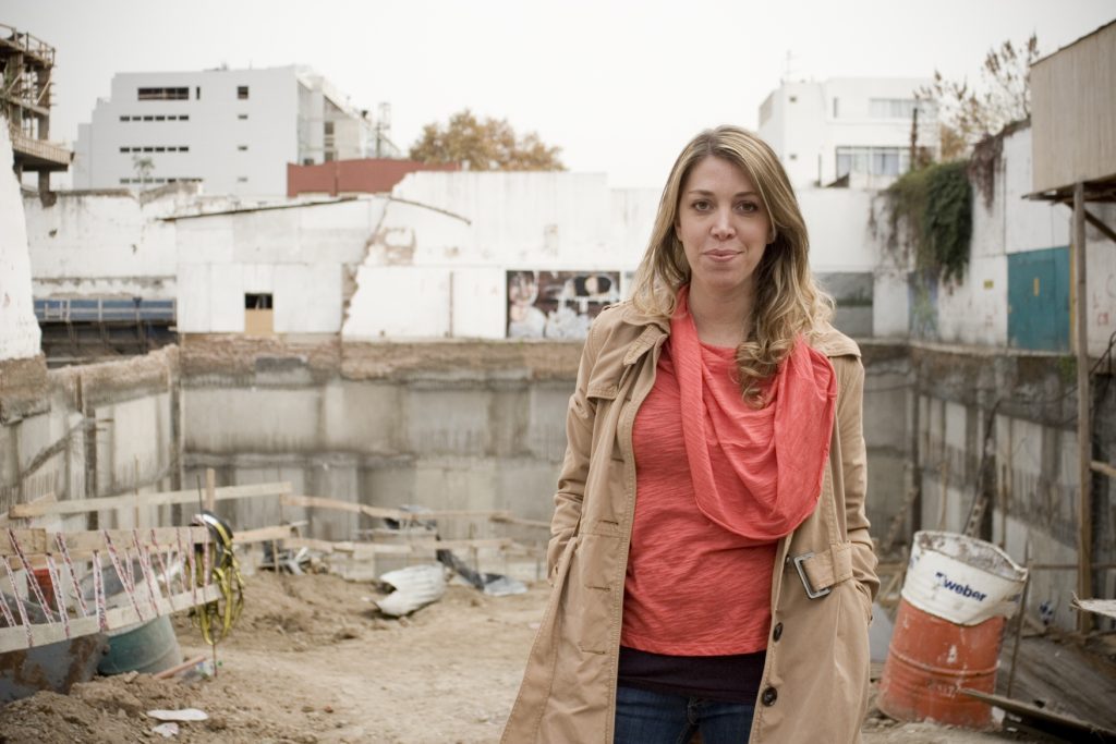 "Wakolda", de Lucía Puenzo: La obsesión por el control de los cuerpos Lucía Puenzo, directora, de pie en una azotea con edificios al fondo, vistiendo blusa roja y cardigan beige