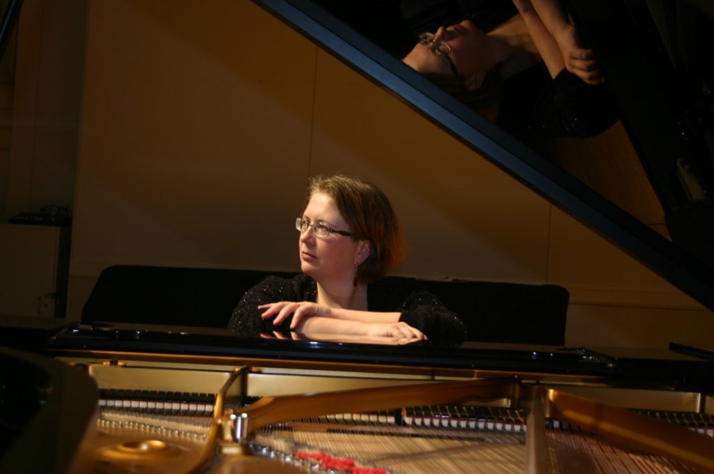 Svetlana Kotova sentada al piano de cola durante una presentación, con gafas y concentrada en la interpretación