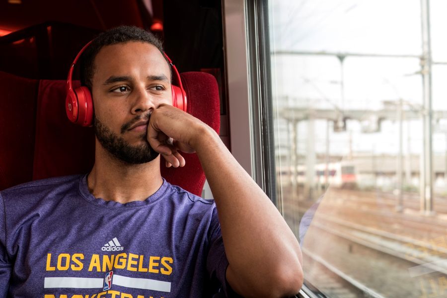 Hombre con auriculares rojos pensativo mirando por ventana de tren, camiseta Los Angeles, ambiente interior de vagón