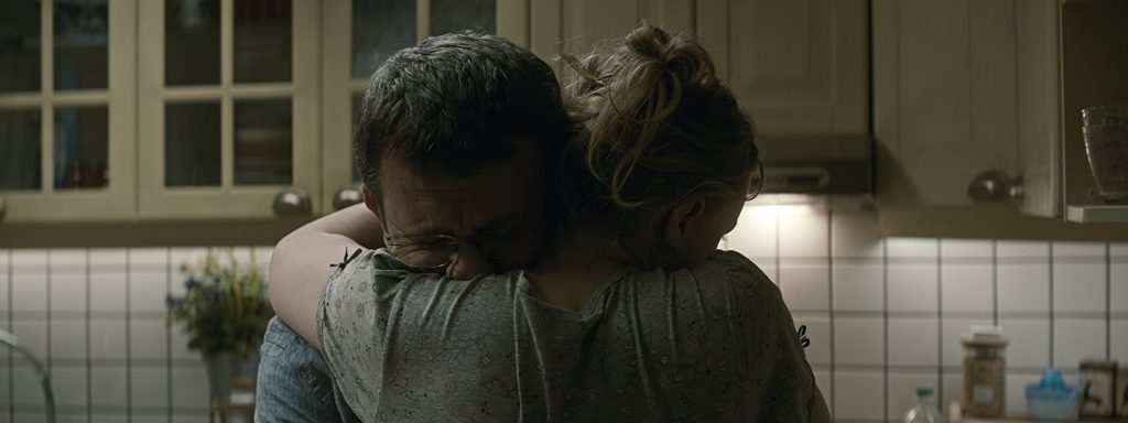 “Graduación”, de Cristian Mungiu: La ética cercada o el éxtasis individual Dos personas abrazadas de espaldas en una cocina de azulejos blancos, escena íntima que sugiere despedida