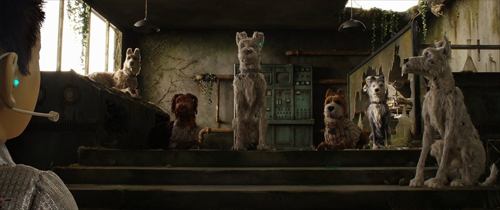 Escena de cine de animación stop-motion: perros en un ambiente urbano deteriorado, con arquitectura industrial y luz