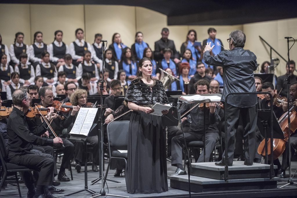 Concierto 6 del Ceac de la Universidad de Chile: La voz voluminosa y bella de la mezzo Nora Sourouzian Director de orquesta dirigiendo a músicos y coro en concierto de la Universidad de Chile con mezzo Nora Sourouzian
