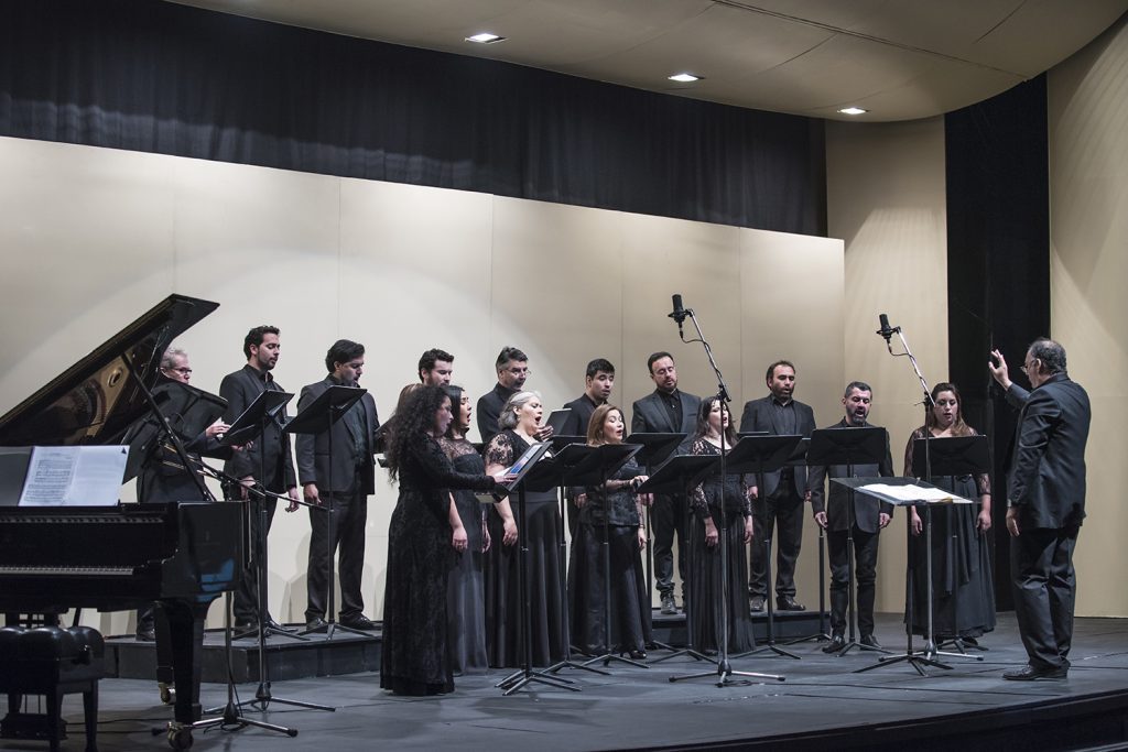 Camerata vocal de la Universidad de Chile en concierto, músicos en escena con partituras y piano de fondo