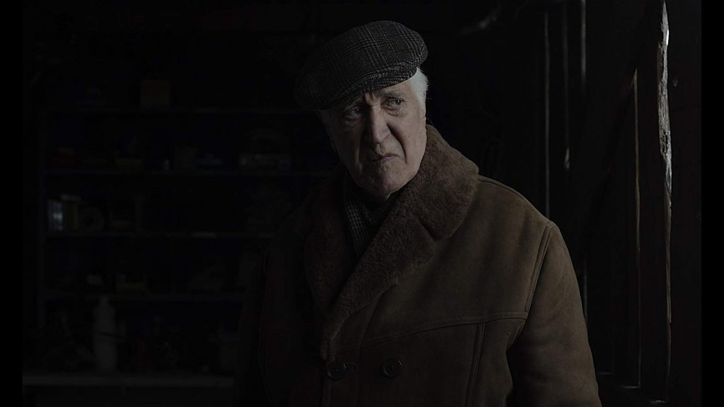 Fragmento de la novela “Informe sobre la muerte de Manuel Quiroz”, de Carlos Zúñiga: En la penumbra de los sentimientos Hombre de mediana edad en ambiente oscuro, vestido con abrigo marrón, mirando hacia un lado con expresión seria