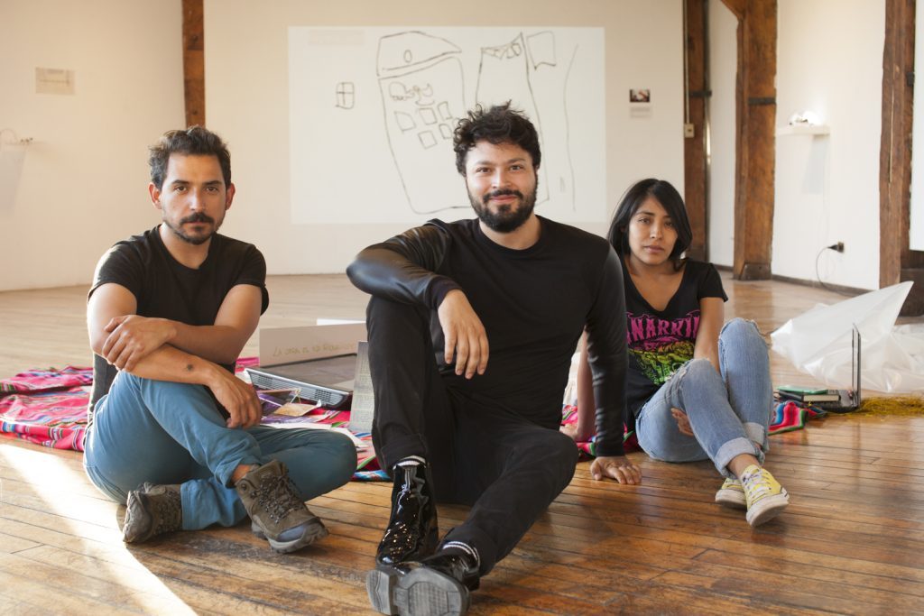Muestra "De Santiago a Santiago": La experiencia estética de "lo aymara" en pleno corazón de la capital chilena Tres integrantes del Colectivo M.A.L. sentados en el piso de un espacio de ensayo, rodeados de materiales de trabajo