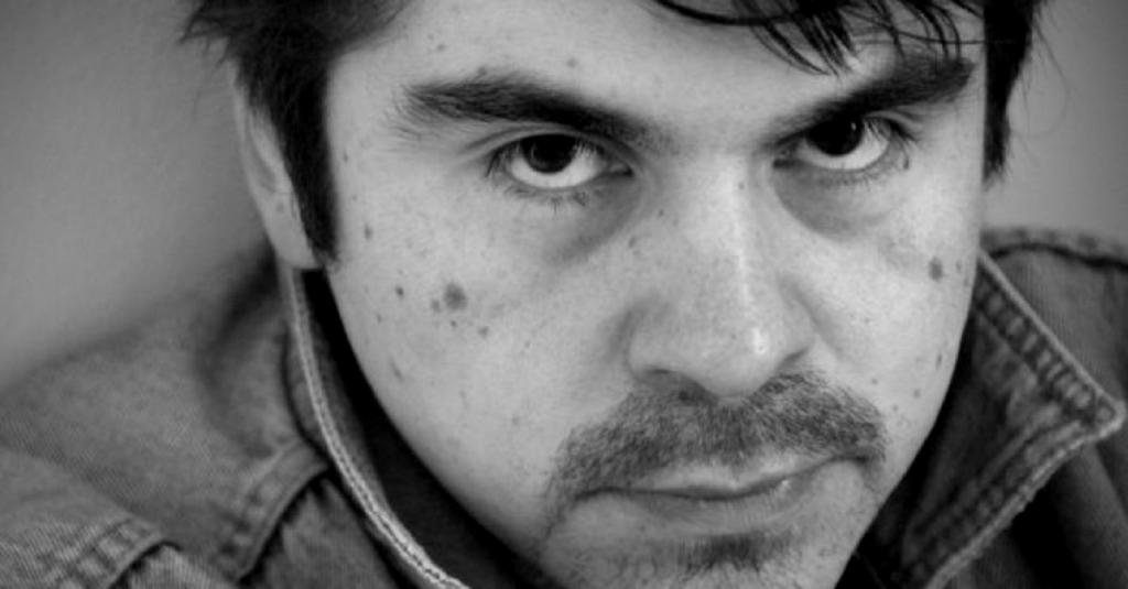 Retrato en blanco y negro del escritor chileno Héctor Hernández Montecinos, con expresión seria y mirada directa