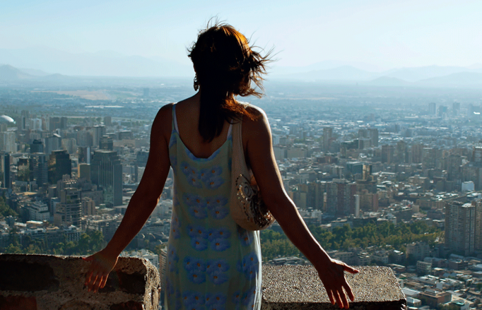 Mujer de pie en mirador elevado observando ciudad panorámica, brazos abiertos hacia el horizonte urbano