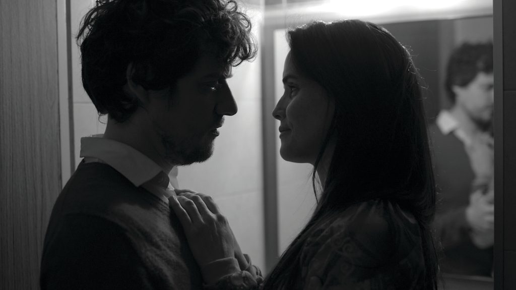 Dos jóvenes se miran frente a frente en blanco y negro, en una escena íntima de tensión emocional dentro de un espacio