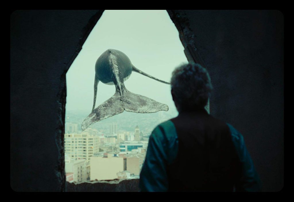Persona de espaldas observando a través de una ventana una figura solitaria en un paisaje desolado y urbano