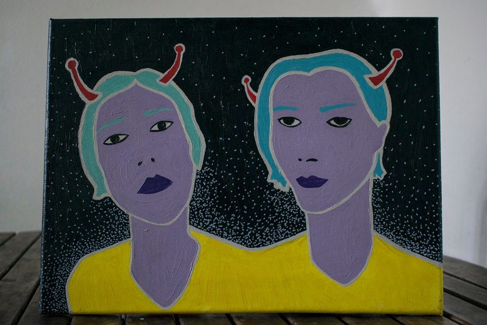 Dos cabezas androides simétricas de piel púrpura con cuernos rojos, torso amarillo y fondo negro estrellado
