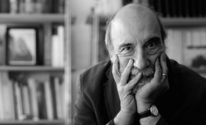 Raúl Zurita, poeta chileno, retrato en blanco y negro con la mano en el rostro, biblioteca al fondo