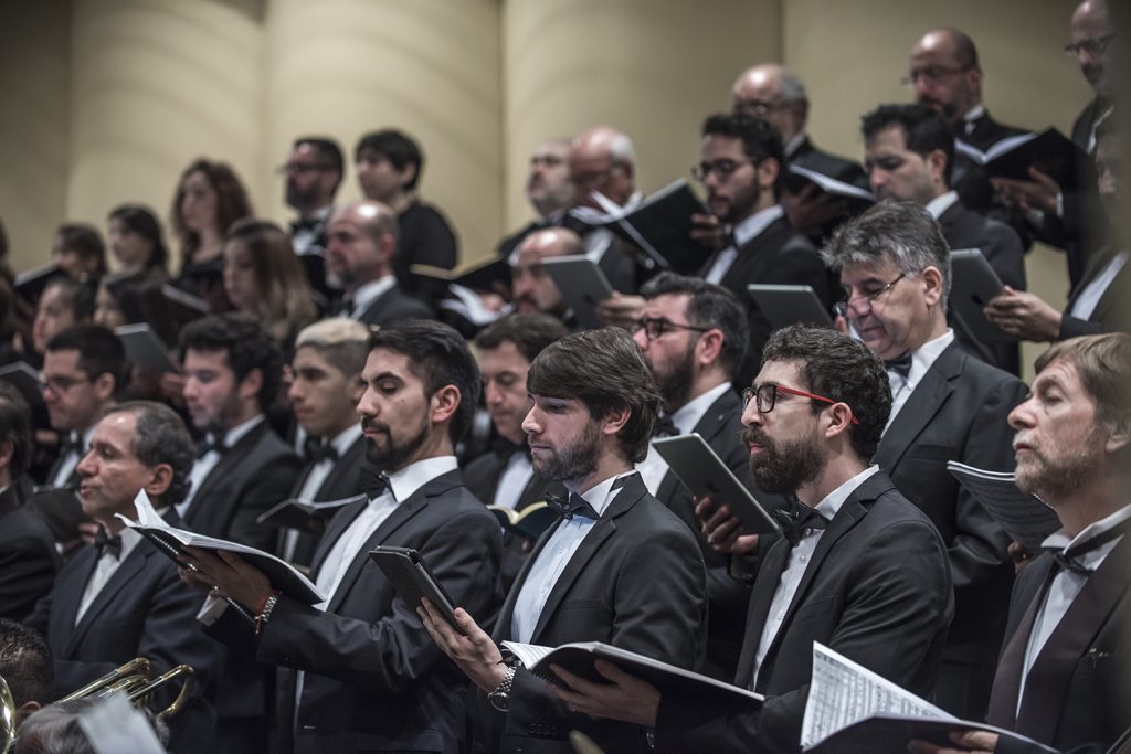 Coro sinfónico en formación, cantantes con partitura en manos durante concierto de música clásica