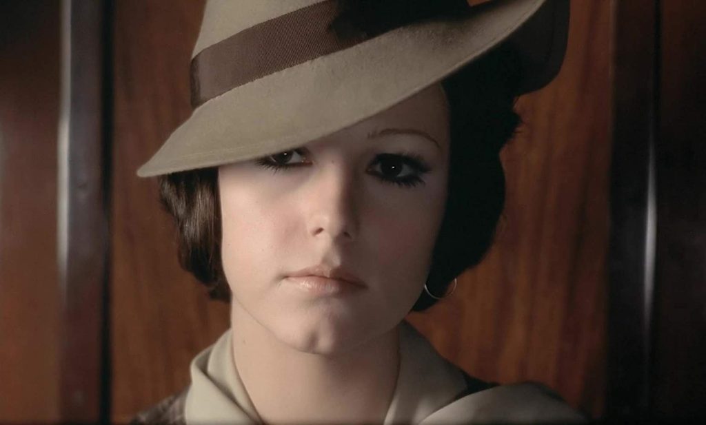 Joven con sombrero de ala ancha y abrigo claro, expresión seria, en escena de El conformista de Bertolucci